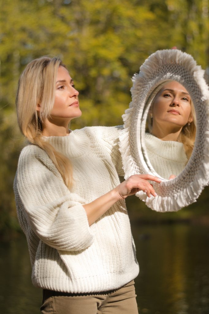 A woman looks at her reflection in the mirror in the autumn forest.Autumn, psychological concept.