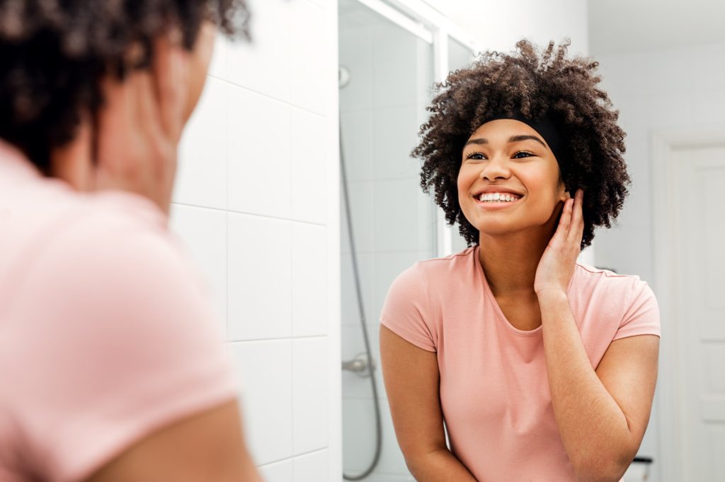 Happy young woman standing in front of mirror in bathroom